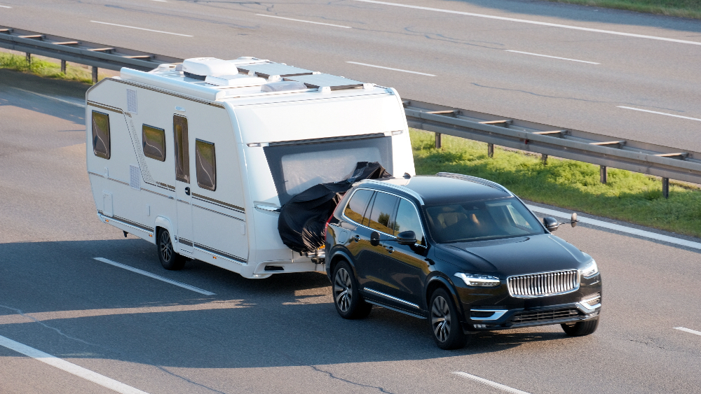 A black SUV towing a white RV on the highway.